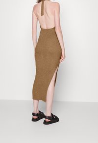 Brun ribbad stickad klänning med halterneck och sidan slit, med en rygglös design och matchad med svarta sandaler.