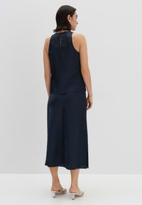 Navyblauw mouwloos top met een textuurafwerking en een sleutelgaatjesdetail aan de achterkant, gecombineerd met een bijpassende enkellange rok. Zilveren sandalen met hak.