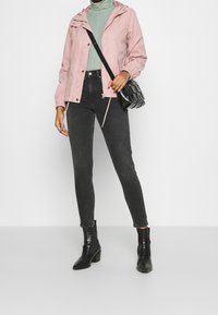 Ljusrosa huva jacka, grå rullkrage, svarta slim fit jeans och svarta ankelstövlar. Accenterad med en strukturerad svart crossbody-väska.