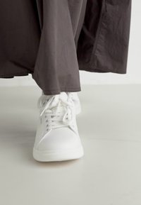 Białe skórzane sneakersy o gładkim wykończeniu, z sznurówką i gumową podeszwą, zestawione z długą, ciemną materiałową spódnicą.