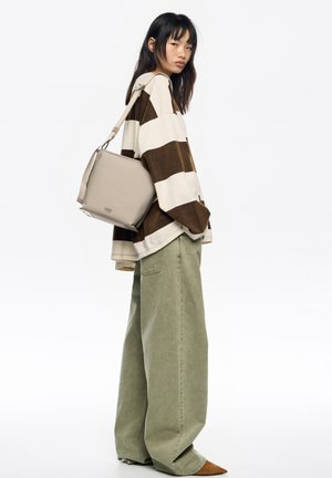 Bolso beige con forma rectangular y correa ajustable, llevado sobre un suéter a rayas marrón y blanco y pantalones anchos de color verde oliva.
