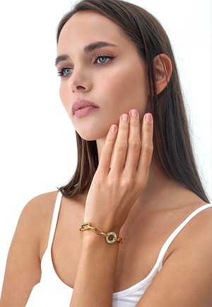 Bracciale d'oro con un link circolare e accenti azzurri. Texture liscia, design a catena intrecciata. Indossato al polso di un modello.