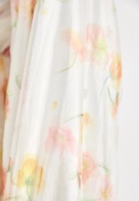 Pañuelo ligero y transparente en color blanco, con suaves patrones florales en tonos pastel de rosa y amarillo, y una textura suave.