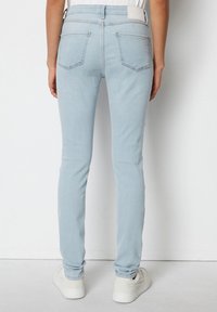 Jeans skinny de color azul claro hechos de mezclilla, con una cintura alta, dos bolsillos traseros y detalles de costura sutiles. Combinados con zapatillas blancas.