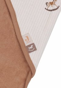 Couverture en coton pour bébé avec un côté texturé brun et un côté côtelé blanc présentant un motif de cheval à bascule. Comprend une étiquette de marque.