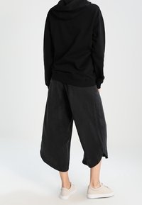 Zwarte hoodie met een comfortabel ontwerp, gecombineerd met brede zwarte culottes met een zachte textuur. Lichtgekleurde sneakers maken de outfit compleet.