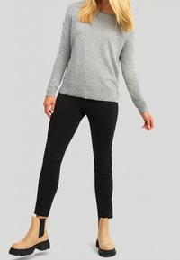 Grauer Langarm-Pullover, schwarze Slim-Fit-Hose und beigefarbene Knöchelschuhe mit schwarzen Sohlen. Weicher Stoff und entspannte Passform.