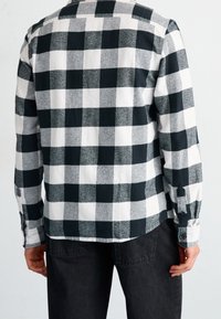 Camicia di flanella a quadri bianco e nero con maniche lunghe, polsini con bottoni e orlo curvo, realizzata in un tessuto morbido e texturizzato.