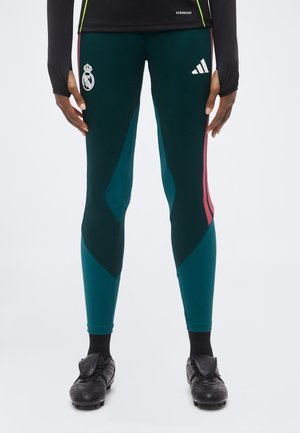 Atlet iført turkis og sorte Adidas sportstights med Real Madrid og Adidas logoer, sorte fodboldstøvler og en sort langærmet top.