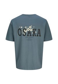 Zila kokvilnas T-kreklu ar vārdu "OSAKA" lielā melnā fontā un ziedu dizainu. Aizmugures skatā centrēta teksts un grafika.