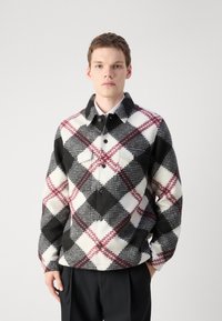 Checkered flannel jacket in black, white, and burgundy. Features a pointed collar, two front pockets, and button closure. Soft texture.