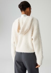 Cremiger, flauschiger Hoodie mit weicher Textur, kurzem Schnitt und Kapuze. Kombiniert mit grauen, hoch taillierten Hosen, zeigt einen lässigen Stil.