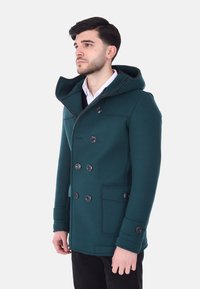 Cappotto doppiopetto turchese con cappuccio, caratterizzato da grandi bottoni neri, tasche laterali e una silhouette sagomata. Tessuto liscio e testurizzato.