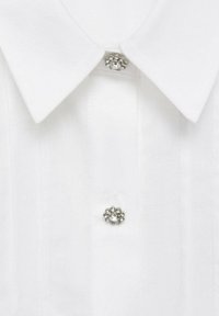 White collared shirt with a textured surface, featuring a floral-shaped silver button with a central rhinestone accent.