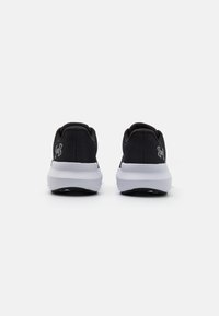 Baskets de sport noires avec une tige en maille texturée et une semelle blanche. Présente un détail de logo sur le talon et un design de bout rond.