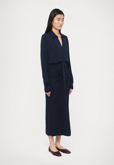 Rochie bleumarin cu mâneci lungi, guler, nasturi în față și un detaliu cu nod răsucit în talie. Material neted, design minimalist.