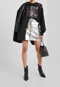 Giacca camicia in pelle nera, felpa grafica nera, mini gonna in metallo argento con zip frontale, stivaletti neri alla caviglia, borsa a tracolla con borchie.