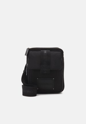 Kompakte schwarze Umhängetasche mit Fronttasche mit Klappe, Reißverschluss-Hauptfach und verstellbarem Schulterriemen mit Markenlogo.