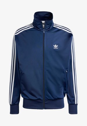 Giacca da allenamento Adidas blu navy realizzata in tessuto morbido, con colletto alto, zip completa e tre strisce bianche su ciascun maniche.