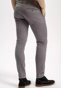 Szare dopasowane spodnie o gładkiej fakturze, z dwoma tylniami kieszeniami i skórzaną metką marki na pasku. Noszone z czarnymi butami.