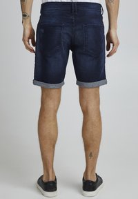 Shorts de mezclilla oscura con puños doblados, que cuentan con dos bolsillos traseros y una cinturilla de media altura. Llevados con zapatillas negras.