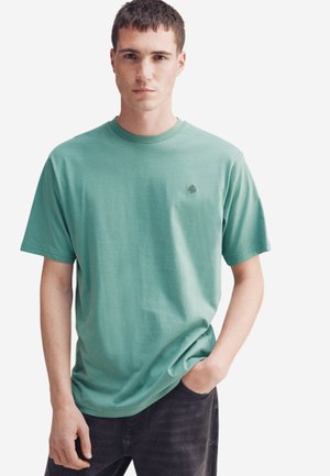 Hellgrünes Baumwoll-T-Shirt mit Rundhalsausschnitt, kurzen Ärmeln und kleinem Logo auf der linken Brust. Der Stoff sieht glatt und weich aus.