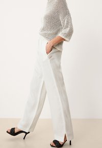 Vita linnbyxor med vida ben, sid fickor och sprund, parat med en löst stickad, kort topp med ett geometriskt mönster i neutrala toner.