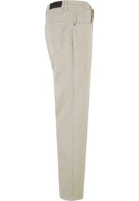 Pantalon beige slim-fit présenté en vue latérale avec poches avant et arrière, passants de ceinture et une petite étiquette noire sur la ceinture.