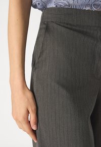 Gray pinstriped trousers made from a textured fabric, featuring side pockets and a tailored fit. Hand resting on the waistband.