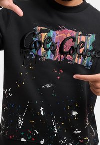 Černá mikina s barevnými skvrnami od barvy, s texturovaným vyšíváním "Cools Col", s přiléhavým výstřihem a dlouhými rukávy.