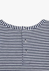 Randig stickad topp i marin och vitt, med rund halsringning och knappstängning bak med tre knappar i silverton.