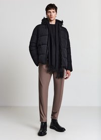 Giacca imbottita nera con cappuccio, maglione grigio lavorato a maglia, sciarpa nera, pantaloni beige e stivaletti neri con finitura testurizzata.