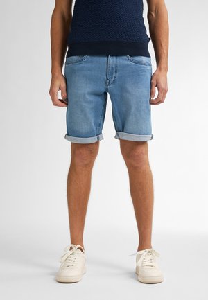 Pantalones cortos de mezclilla de color azul claro con puños doblados, diseño de cinco bolsillos y corte relajado. Combinados con zapatillas de color crema.