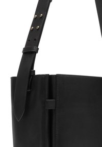 Czarna skórzana torba o gładkiej fakturze, z eleganckim wzornictwem, regulowanym paskiem z metalowymi ćwiekami i przeszywanymi akcentami.