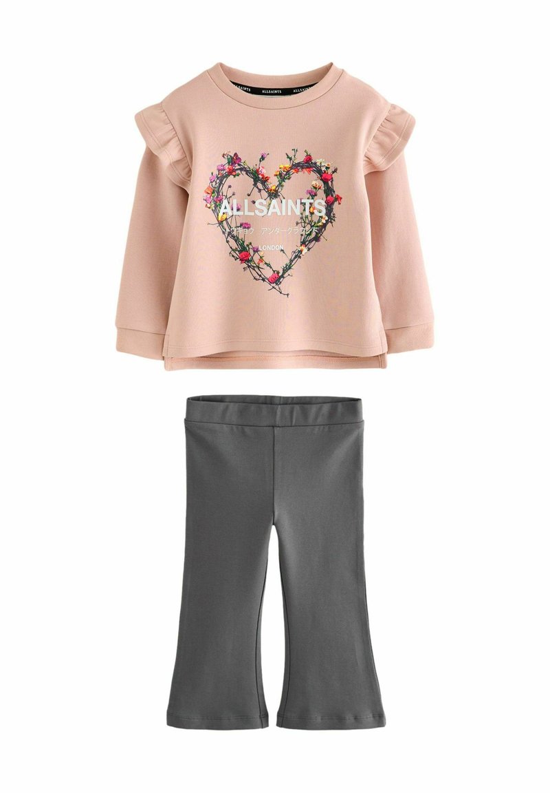 Svetloružové tričko s dlhým rukávom a volánovými rukávmi, zdobené kvetinovým motívom v tvare srdca a textom. Dopĺňajú ho tmavosivé rozšírené legíny.