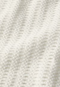 Gros plan sur un tissu tricoté blanc doux avec un motif texturé de boucles verticales et de mailles ouvertes.