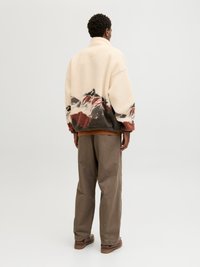 Jachetă din fleece în nuanță crem cu un model montan în tonuri de gri și roșu la margine. Croi lejer, asortată cu pantaloni maronii și încălțăminte.