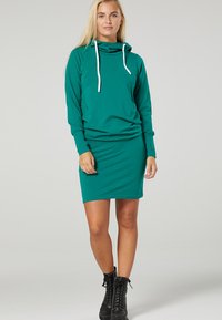 Teales Hoodie-Kleid mit langen Ärmeln, Halspatenkragen, weißen Kordeln und figurbetontem Rock. Hergestellt aus weichem, dehnbarem Stoff; verfügt über Seitentaschen.