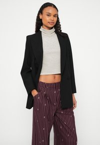 Zwarte op maat gemaakte blazer over een gestreepte cropped coltrui, gecombineerd met wijnrode wijde broek met krijtstreep en een subtiel patroon.
