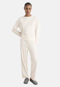 Haut à manches longues blanc et pantalon assorti en tissu doux, avec une coupe décontractée et un design minimaliste. Des chaussons gris complètent le look.