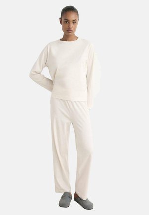 Top blanco de manga larga y pantalones a juego, hechos de una tela suave, con un corte holgado y un diseño minimalista. Pantuflas grises completan el look.