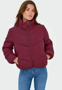 Bordo puffer jakna s visokim ovratnikom, zatvaračem sprijeda i detaljima ševrona. Ima oversized rukave i bočne džepove.