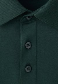 Gros plan d'un polo vert foncé montrant trois boutons noirs et le col côtelé avec des coutures détaillées.