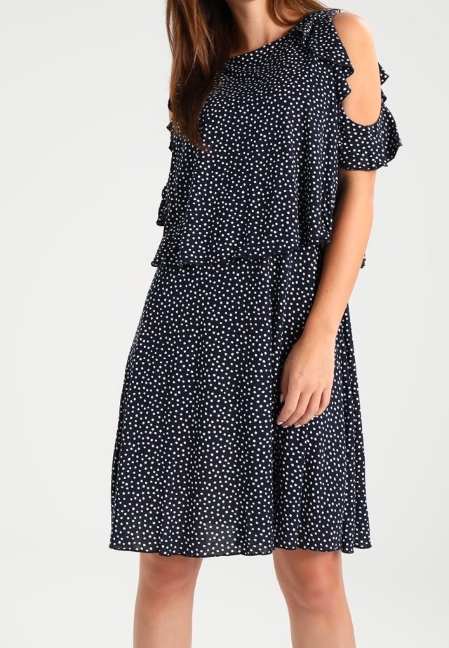 Marineblauwe jurk met witte stippen, voorzien van een off-shoulder ontwerp, gerimpelde mouwen en een vloeiende A-lijn silhouet. Lichtgewicht stof.