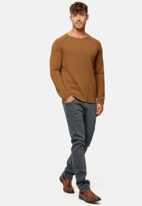 Brun ribbet langærmet skjorte med rund halsudskæring, parret med grå jeans og brune ankelstøvler. Minimalistisk design med tætsiddende struktur.