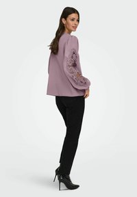 Hele lilla pikkade varrukatega pluus pitsdetailidega varrukatel, kombineeritud mustade kitsaste teksapükstega ja kõrgete kontsadega poolsaabastega.