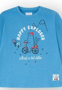 Camiseta azul para niño pequeño con ilustración de un oso con un sombrero rojo montando una bicicleta con un conejo como pasajero, montañas y árboles, texto "Explorador Feliz."