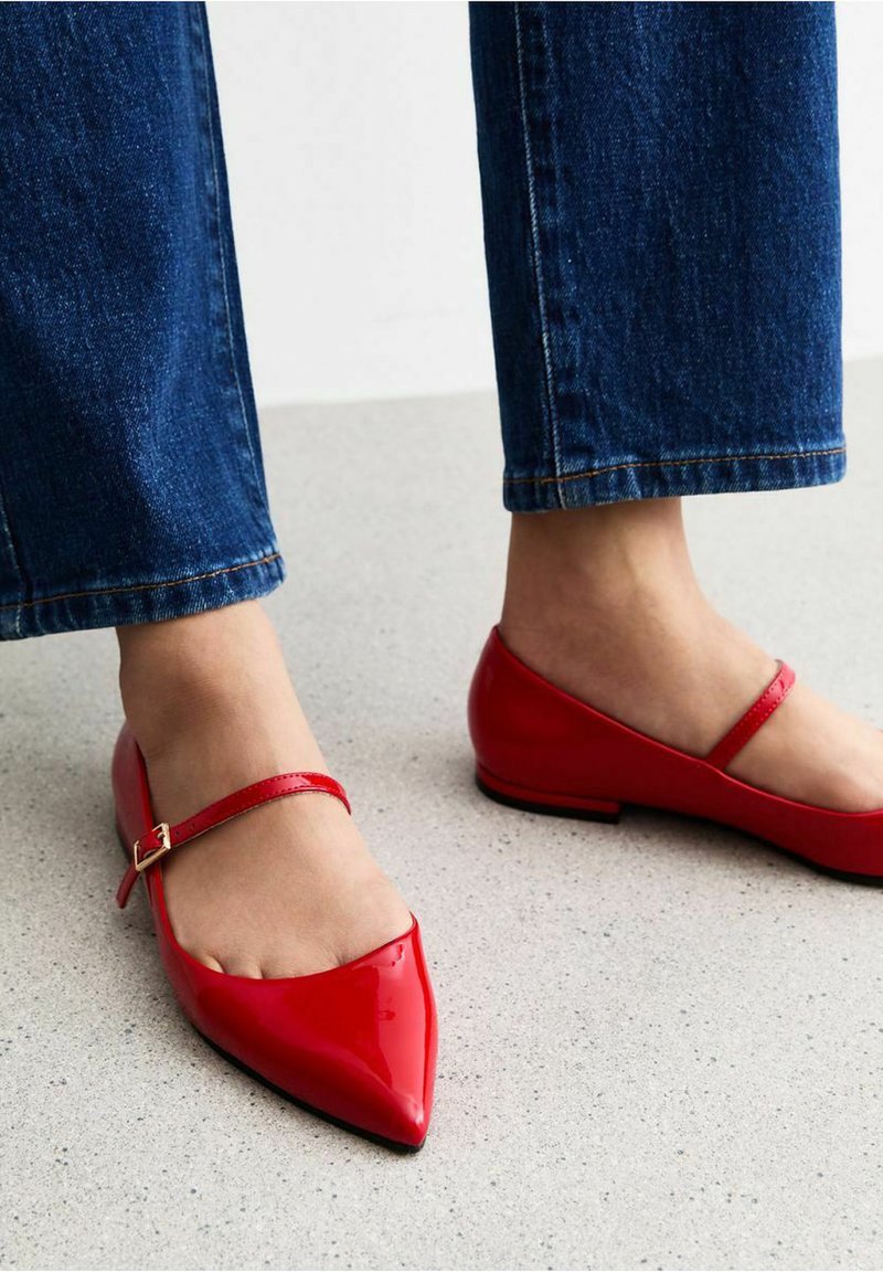 Röda läderballerina med spetsig tå, med ett tunt vristband och en låg klack, matchade med mörkblå denimjeans.