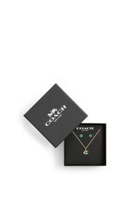 Boîte à bijoux noire Coach avec collier en or et boucles d'oreilles clous assorties avec des pierres circulaires vertes à l'intérieur.