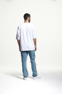Witte oversized t-shirt met korte mouwen, gecombineerd met lichtblauwe denim jeans en witte sneakers, gezien van achteren tegen een neutrale achtergrond.